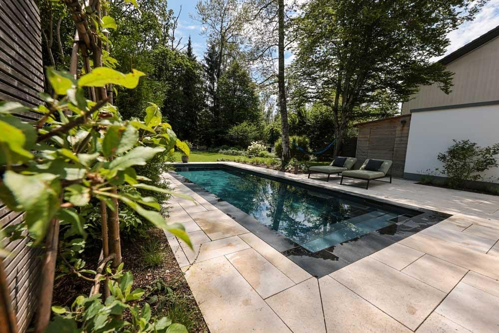 Designpool Naturpool mit Liegen und heller Steinterrasse im Garten