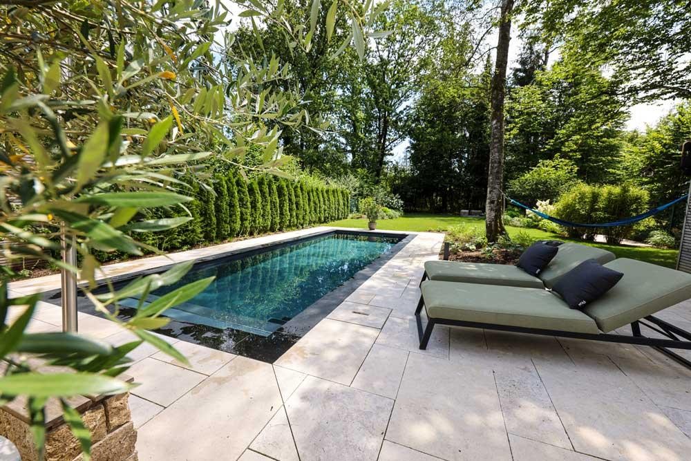Designpool Naturpool mit heller Steinterrasse und Liegen im ruhigen Garten