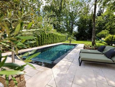 Designpool Naturpool mit heller Steinterrasse und Liegen im ruhigen Garten