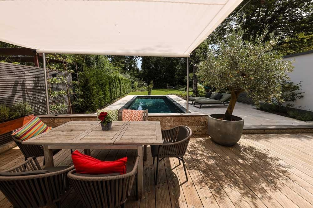 Designpool Naturpool mit Holzterrasse sowie Sonnensegel und Essplatz im Garten