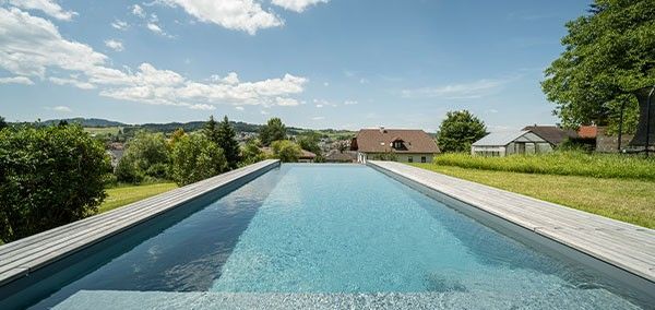 Living Pool im Garten mit klarer Wasseroberflaeche und Ausblick Living Pool mit klarer Wasseroberflaeche und Holzumrandung in einem Garten mit Ausblick auf die Landschaft