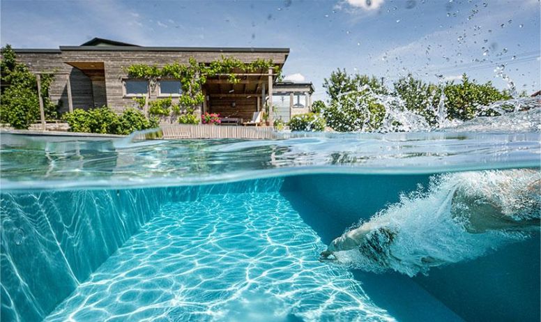 Chlorfreies kristallklares Wasser in einem Biotop Naturpool mit Unterwasserblick und schwimmender Person im Garten