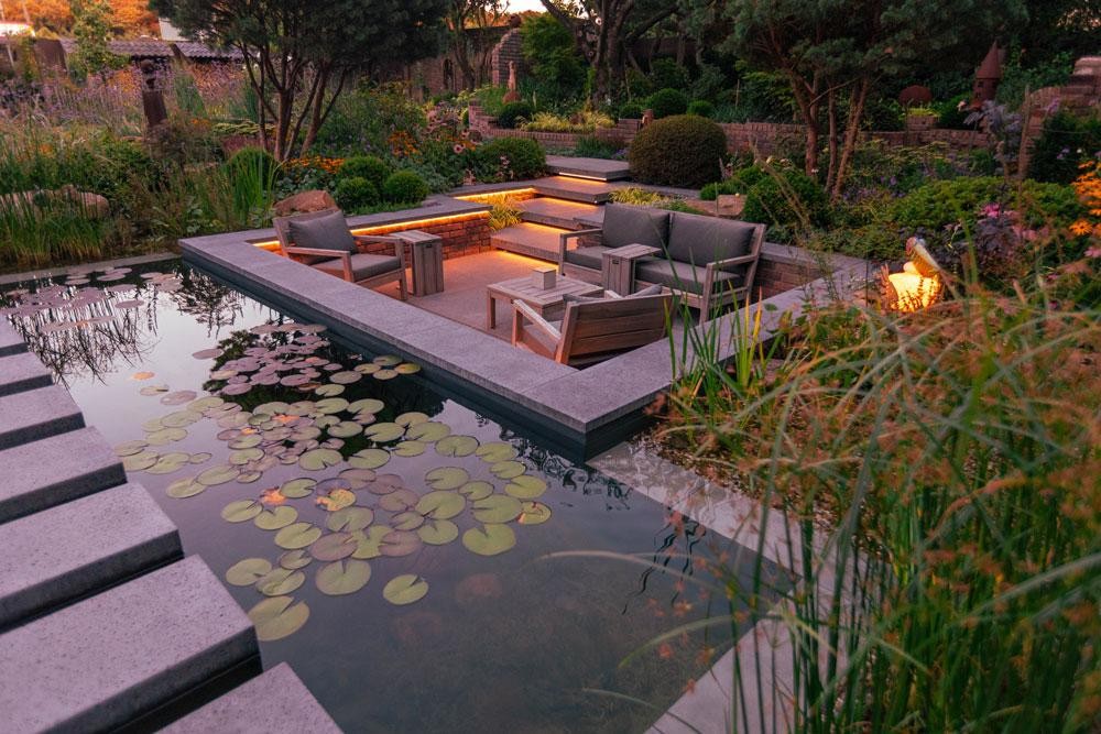 Lounge am Naturpool mit Seerosen und warmer Abendbeleuchtung