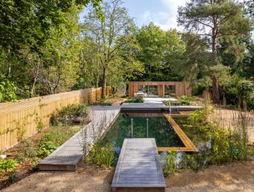 Naturpool mit Holzdeck in großem Stadtgarten vor Backsteinhaus