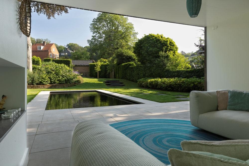 Blick aus der Lounge auf Naturpool, Terrasse und grünen Garten