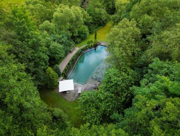 Luftaufnahme eines natuerlichen Schwimmteich umgeben von Baeumen und Natur