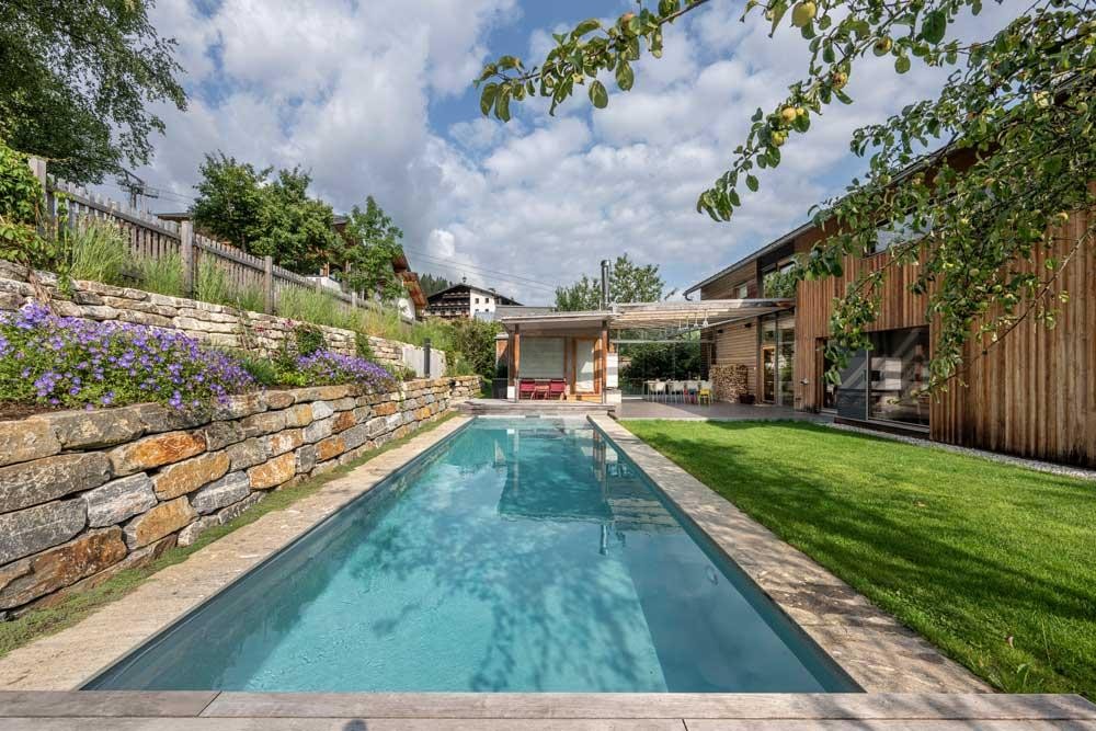 Moderner Biopool im Garten mit Holzhaus und Natursteinmauer