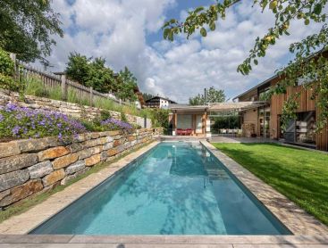 Moderner Biopool im Garten mit Holzhaus und Natursteinmauer