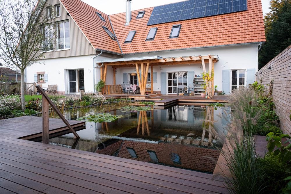 Naturpool mit Holzterrasse modernem Haus und Solardach