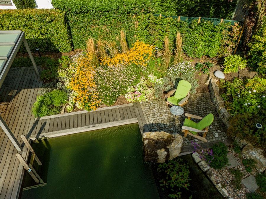 Sitzplatz am Schwimmteich mit Bluetenbeet und gruenen Sesseln