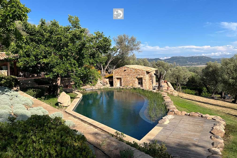 Schwimmteich mit Holzdeck und Steinhaus in Hanglage mit Panoramablick