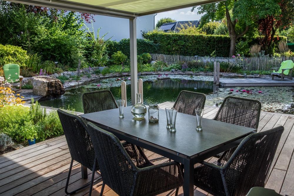 Terrasse mit Esstisch und Blick auf Schwimmteich im Naturgarten